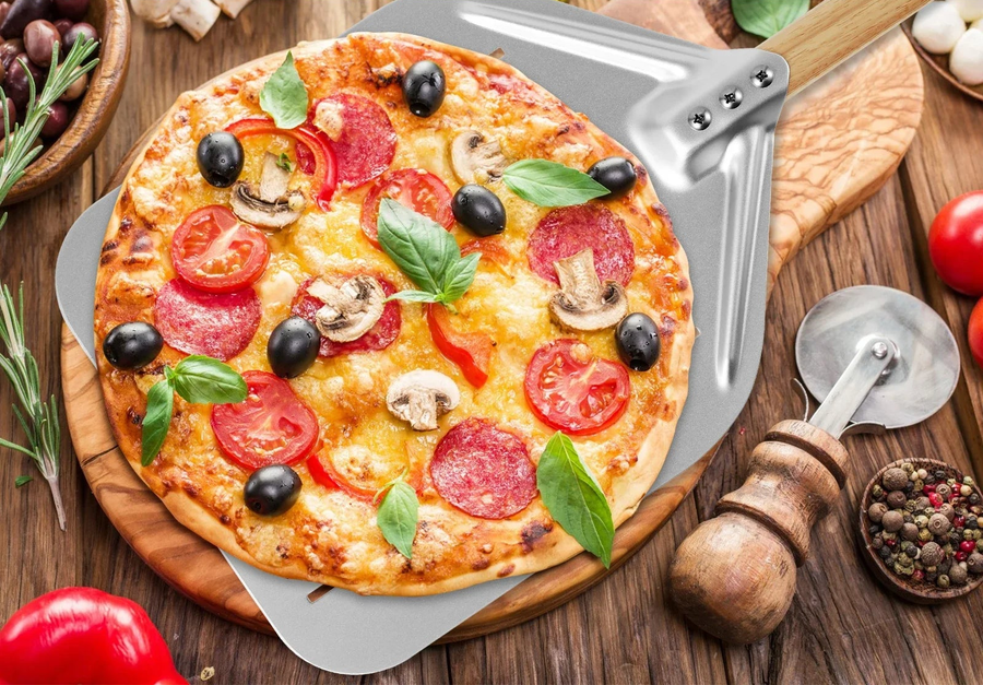 Metal pizza peel with wood handle beside a fresh baked pizza on a wooden board